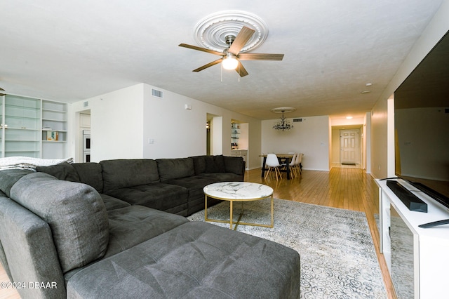 living room with ceiling fan with notable chandelier, light wood-type flooring, and a textured ceiling