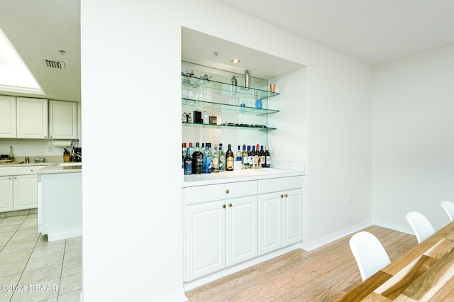 bar with light hardwood / wood-style floors and white cabinetry