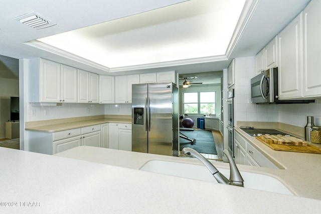 kitchen featuring ceiling fan, a raised ceiling, white cabinetry, and stainless steel appliances