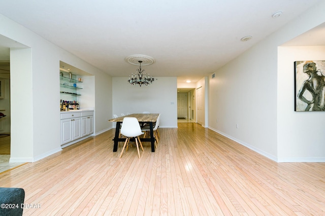 dining area featuring bar area, light wood-type flooring, and an inviting chandelier