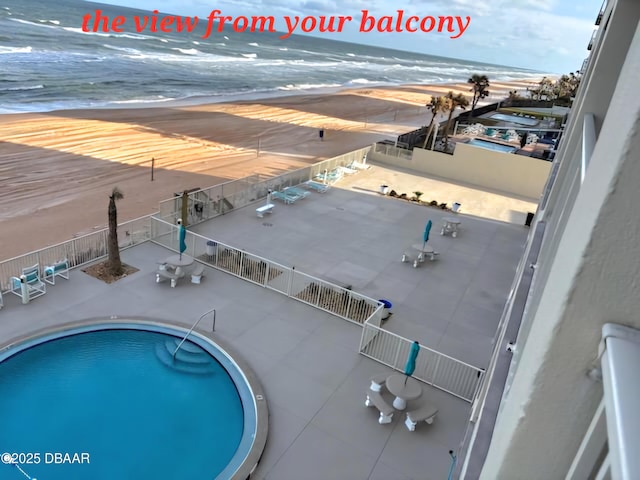 view of swimming pool with a patio, a water view, and a beach view