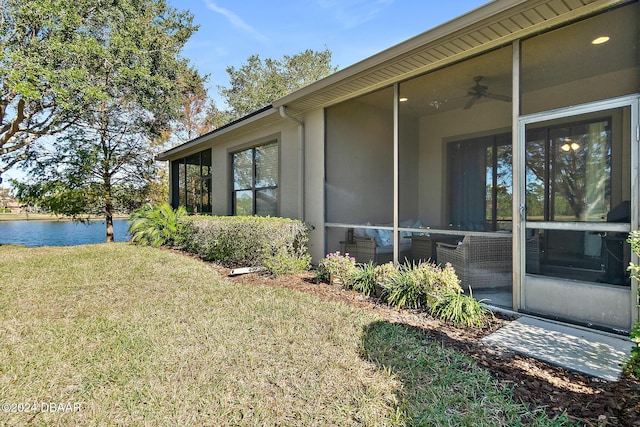 view of side of property with a yard, a water view, ceiling fan, and a sunroom