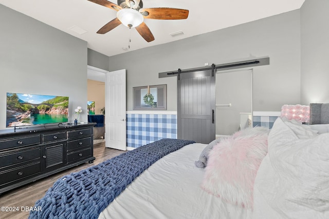 bedroom with a barn door, ceiling fan, and hardwood / wood-style floors