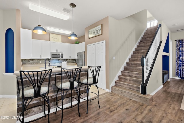 kitchen with hanging light fixtures, stainless steel appliances, backsplash, white cabinets, and light wood-type flooring