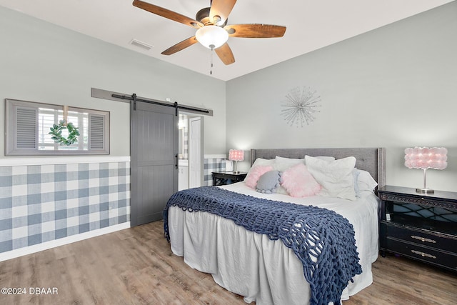 bedroom with ceiling fan, a barn door, and wood-type flooring