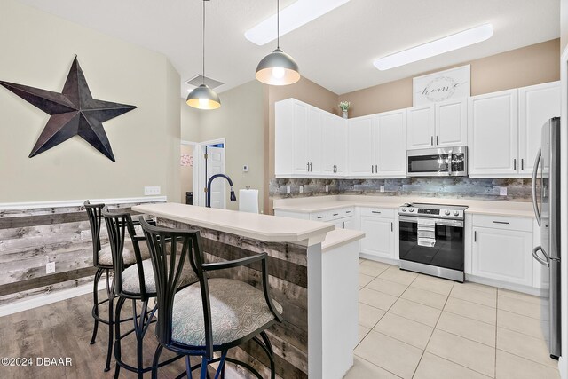 kitchen with white cabinetry, hanging light fixtures, stainless steel appliances, decorative backsplash, and light tile patterned flooring