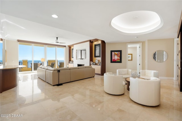 living room featuring ceiling fan, a wall of windows, a tray ceiling, and crown molding