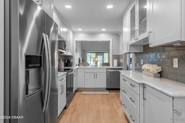 kitchen featuring stainless steel appliances, light hardwood / wood-style floors, backsplash, crown molding, and white cabinets