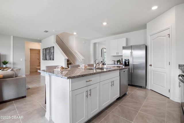 kitchen with light tile patterned flooring, white cabinetry, stainless steel appliances, light stone countertops, and a kitchen island with sink