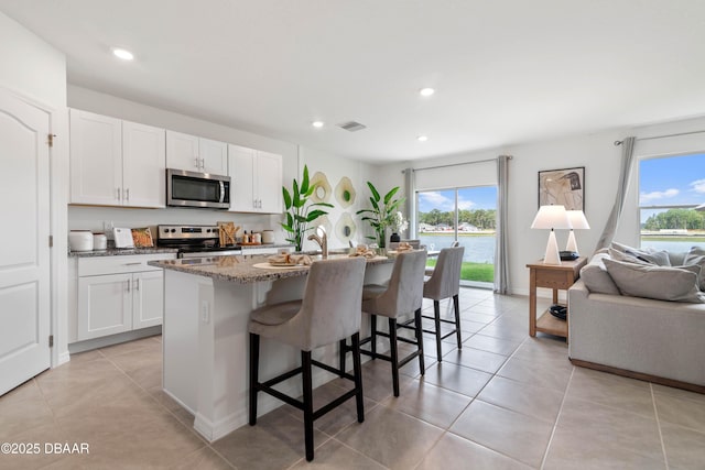 kitchen featuring a breakfast bar area, appliances with stainless steel finishes, a kitchen island with sink, white cabinetry, and stone countertops