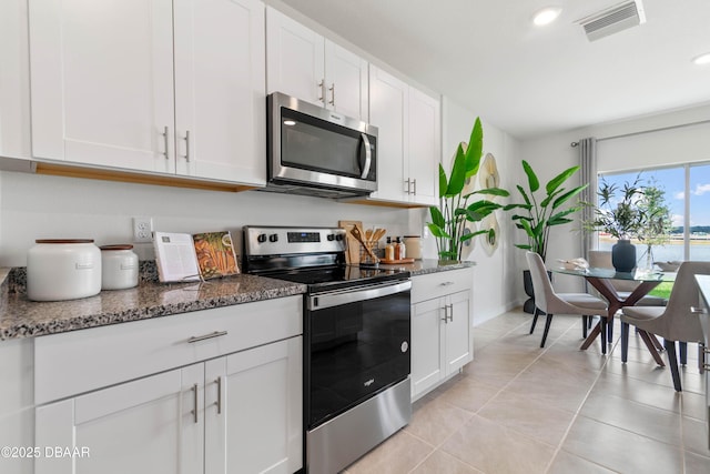 kitchen with light tile patterned flooring, appliances with stainless steel finishes, white cabinets, and dark stone counters