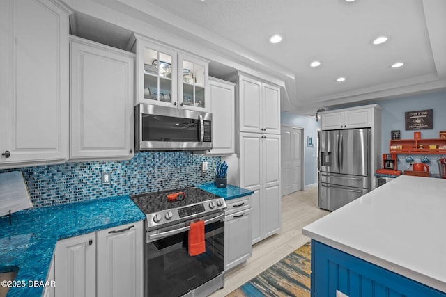 1942 N Daytona Ave, Flagler Beach, FL 32136 - kitchen featuring appliances with stainless steel finishes, white cabinetry, light wood finished floors, tasteful backsplash, and glass insert cabinets