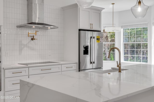 kitchen with wall chimney range hood, a sink, decorative backsplash, stainless steel fridge with ice dispenser, and black electric cooktop