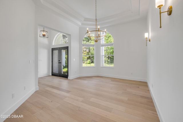 unfurnished dining area with light wood-style floors, a tray ceiling, a towering ceiling, baseboards, and a notable chandelier