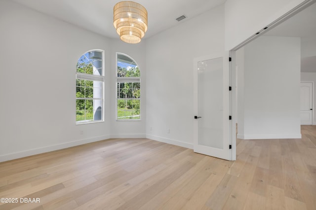 empty room featuring baseboards, a notable chandelier, light wood-style floors, and visible vents