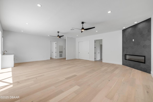 unfurnished living room with baseboards, a large fireplace, light wood finished floors, and recessed lighting