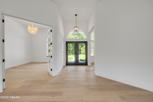 foyer featuring a chandelier, light wood finished floors, baseboards, and french doors