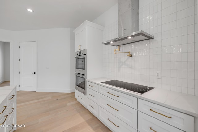 kitchen featuring wall chimney range hood, decorative backsplash, stainless steel double oven, light wood-style floors, and black electric stovetop