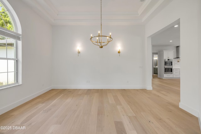 interior space with light wood finished floors, baseboards, a chandelier, crown molding, and a raised ceiling