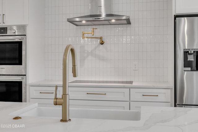kitchen with white cabinets, light stone counters, extractor fan, tasteful backsplash, and appliances with stainless steel finishes