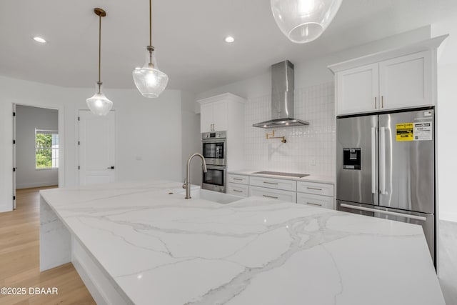kitchen with wall chimney range hood, a sink, light wood-type flooring, white cabinetry, and appliances with stainless steel finishes