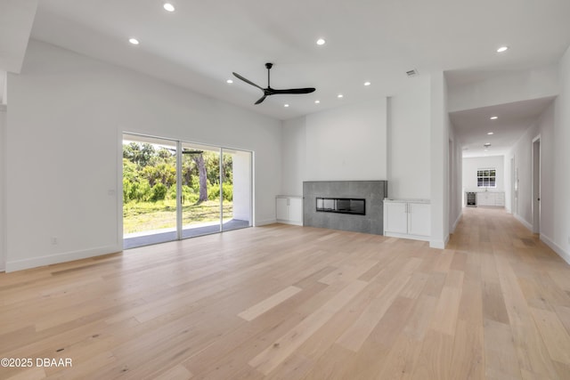 unfurnished living room featuring ceiling fan, a tile fireplace, light wood-style flooring, a high ceiling, and recessed lighting