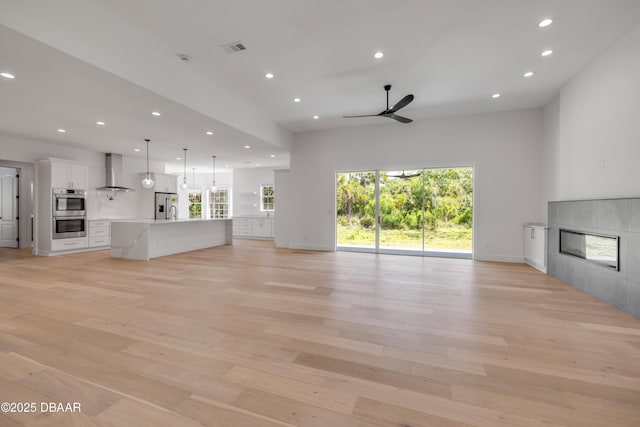 unfurnished living room featuring recessed lighting, light wood finished floors, visible vents, a glass covered fireplace, and ceiling fan