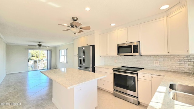 kitchen with a kitchen island, white cabinetry, ornamental molding, stainless steel appliances, and light stone countertops