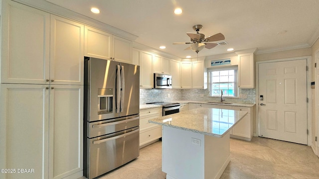 kitchen with appliances with stainless steel finishes, a kitchen island, white cabinetry, sink, and light stone countertops