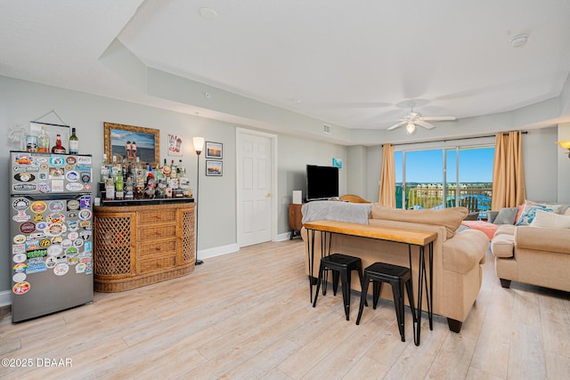 living area with baseboards, ceiling fan, a dry bar, and light wood-style floors