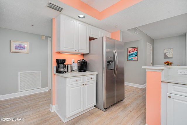 kitchen featuring white cabinetry, stainless steel fridge, visible vents, and light countertops
