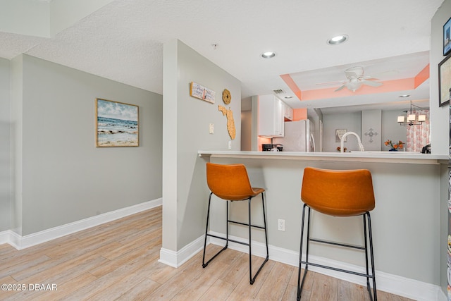 kitchen featuring white cabinets, light countertops, light wood-type flooring, a tray ceiling, and a kitchen bar