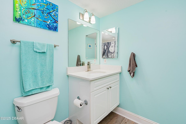 bathroom featuring toilet, baseboards, wood finished floors, and vanity