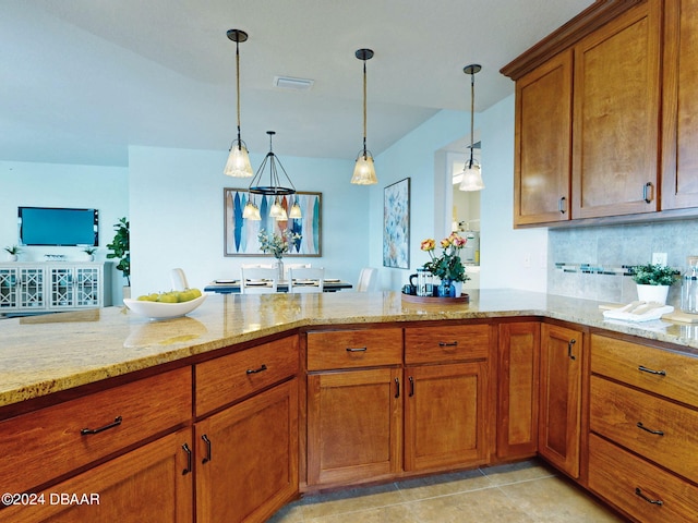 kitchen featuring hanging light fixtures, light stone counters, backsplash, kitchen peninsula, and light tile patterned floors