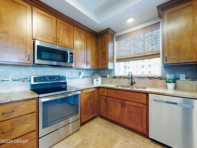 kitchen featuring backsplash, light stone countertops, sink, and stainless steel appliances