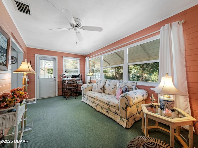 living room with wooden walls, carpet flooring, visible vents, and ceiling fan