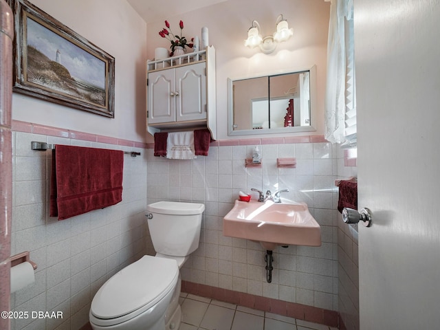 bathroom with a wainscoted wall, a sink, tile patterned flooring, tile walls, and toilet