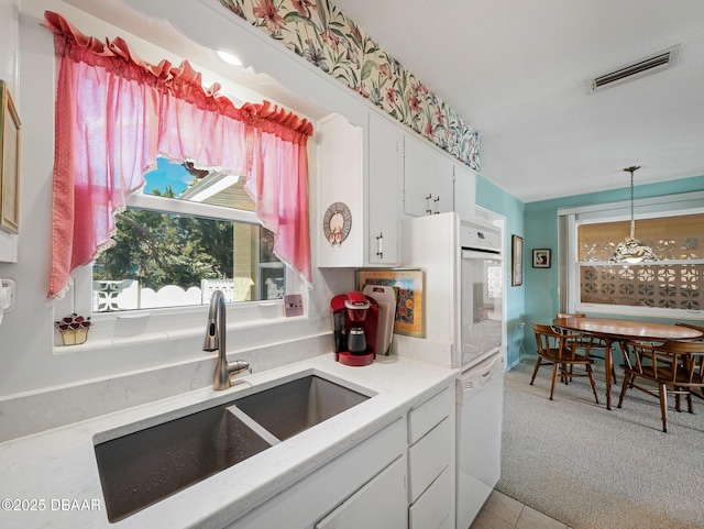 kitchen featuring visible vents, pendant lighting, a sink, white appliances, and light colored carpet