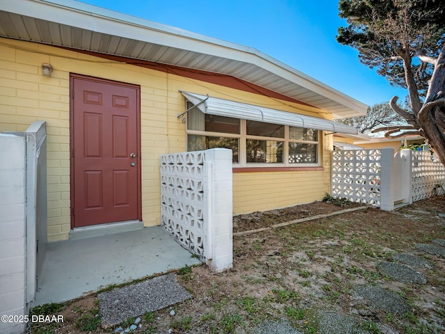 view of exterior entry featuring concrete block siding and fence