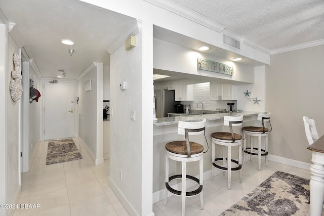 kitchen featuring a breakfast bar, kitchen peninsula, decorative backsplash, light tile patterned floors, and white cabinetry