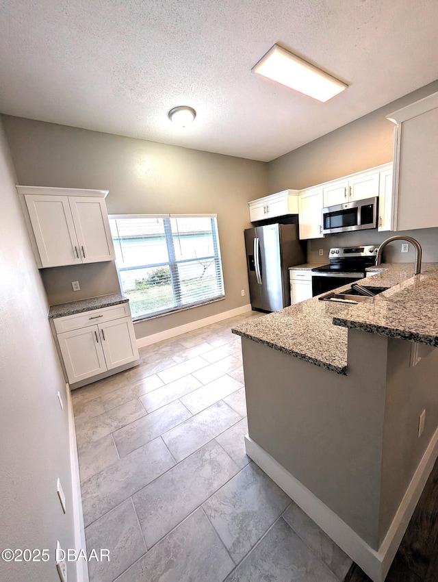 kitchen featuring white cabinetry, appliances with stainless steel finishes, kitchen peninsula, and light stone counters