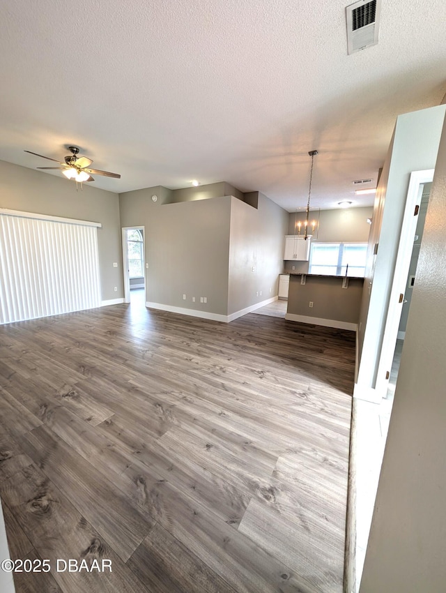 unfurnished living room featuring wood-type flooring, ceiling fan with notable chandelier, and a textured ceiling