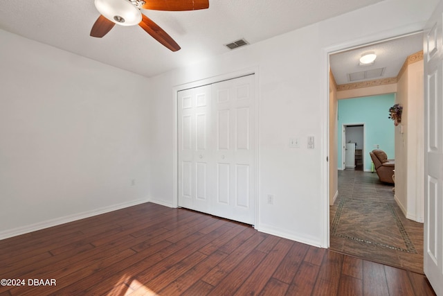 unfurnished bedroom featuring a closet, ceiling fan, a textured ceiling, and dark hardwood / wood-style floors