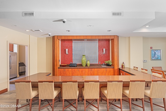 bar featuring stainless steel fridge and light wood-type flooring