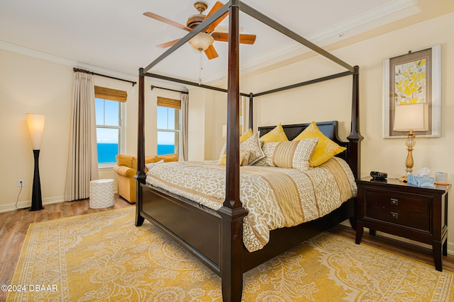 bedroom featuring light hardwood / wood-style flooring, a water view, ceiling fan, and crown molding