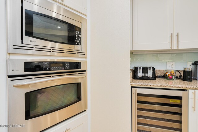 1925 S Atlantic Ave Unit 806, Daytona Beach Shores, FL 32118 - kitchen featuring appliances with stainless steel finishes, wine cooler, white cabinetry, light stone countertops, and decorative backsplash