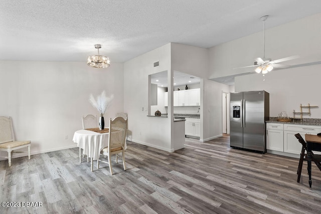 dining space with a textured ceiling, wood-type flooring, and ceiling fan with notable chandelier