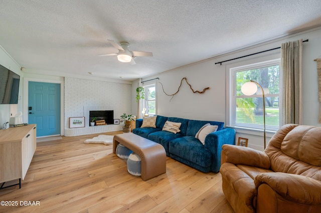 living area with a textured ceiling, a fireplace, a ceiling fan, and light wood-style floors