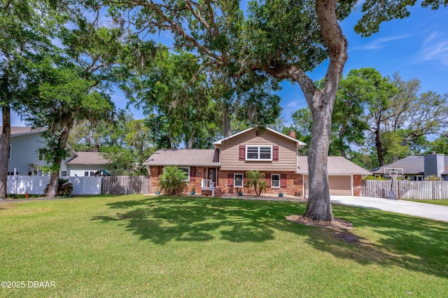 tri-level home featuring a chimney, fence, a front yard, brick siding, and driveway