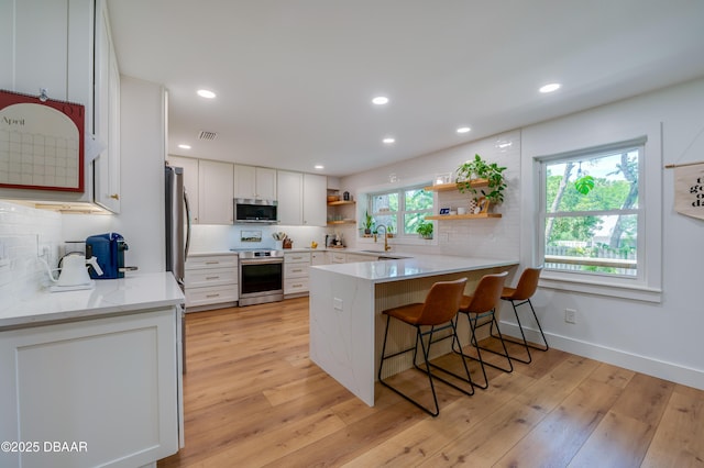 kitchen with a sink, a peninsula, open shelves, decorative backsplash, and appliances with stainless steel finishes